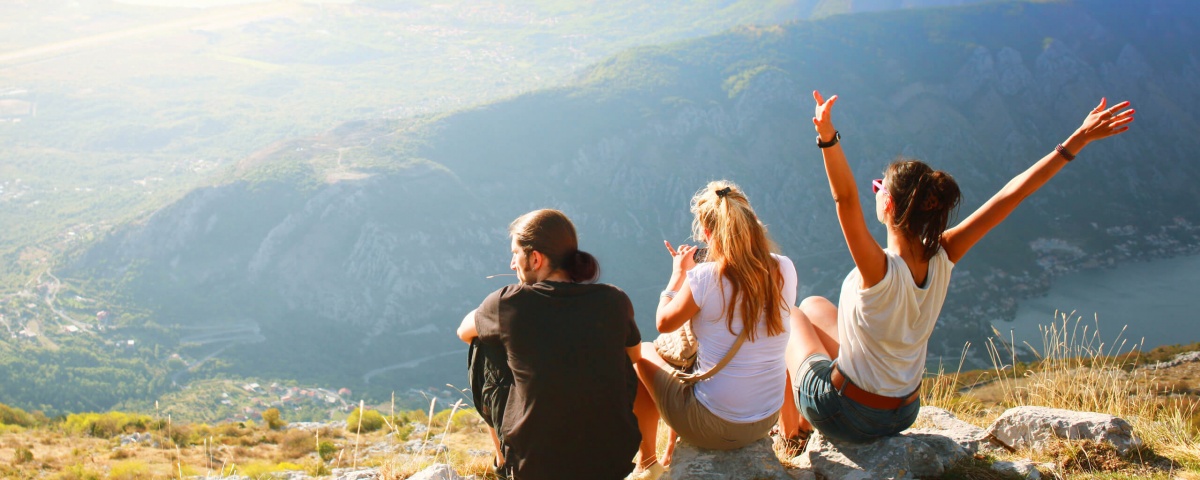 A trio of young adults enjoy the outdoors from the top of a mountain