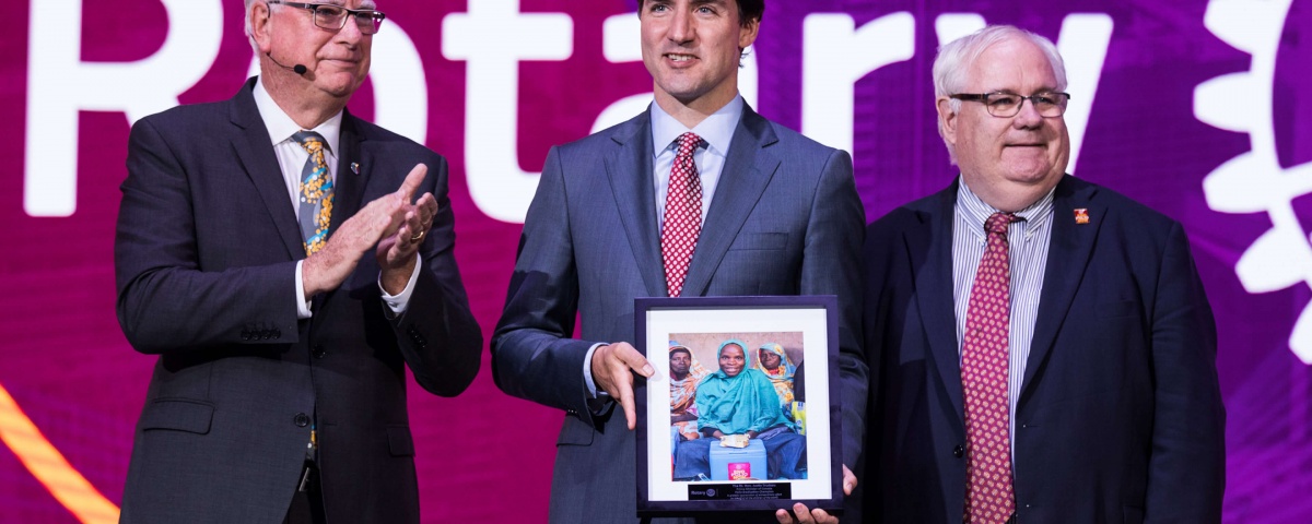 Justin Trudeau on stage with two men at a Rotary International event
