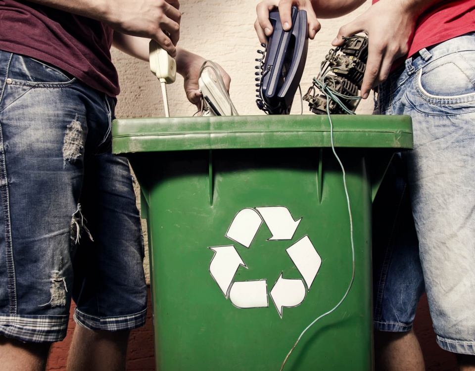 Two people dispose of electronics in a recycling bin