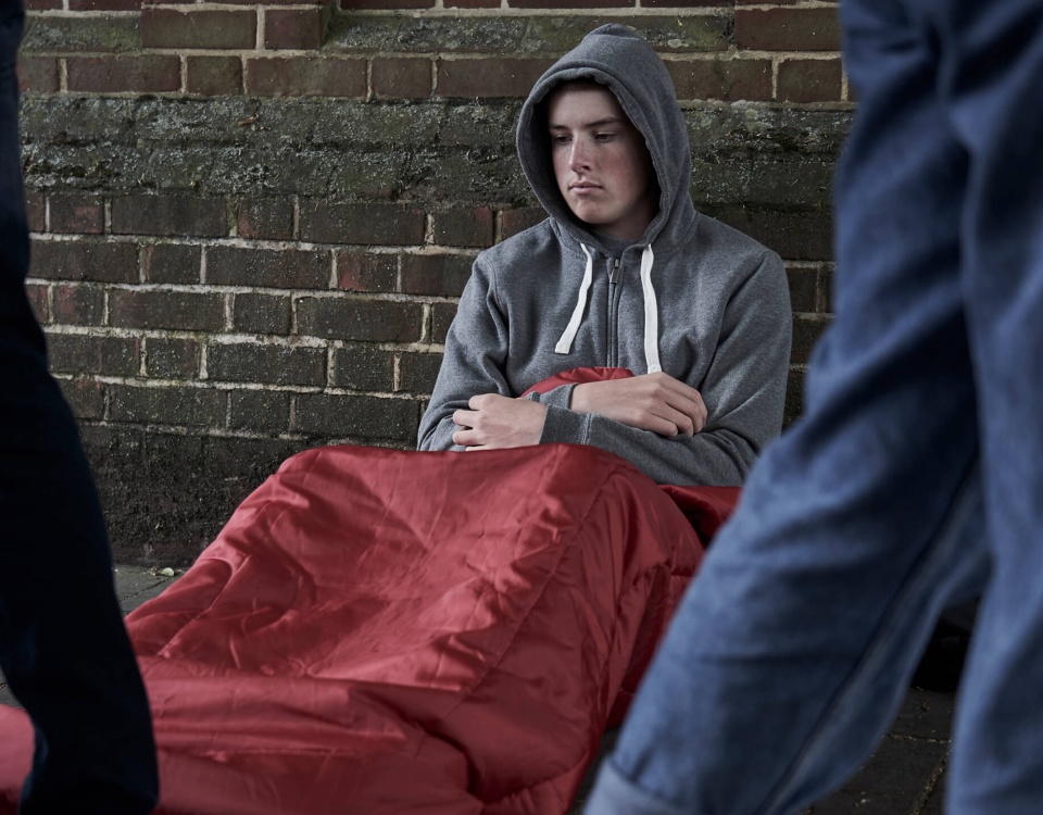 A young man lives on the streets, wrapped in a blanket